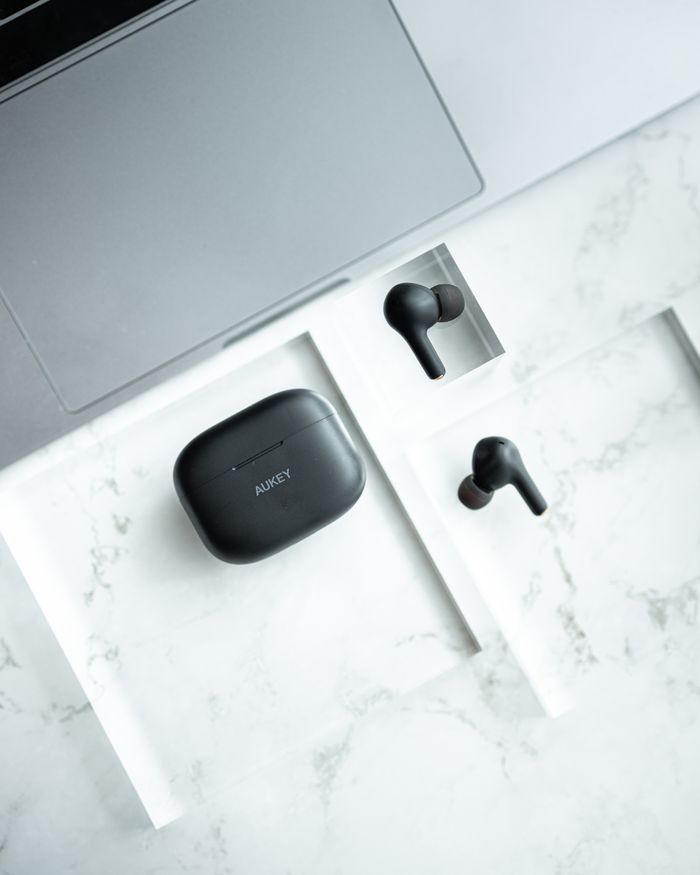 Top view of sleek wireless earbuds and case on a marble surface next to a laptop.